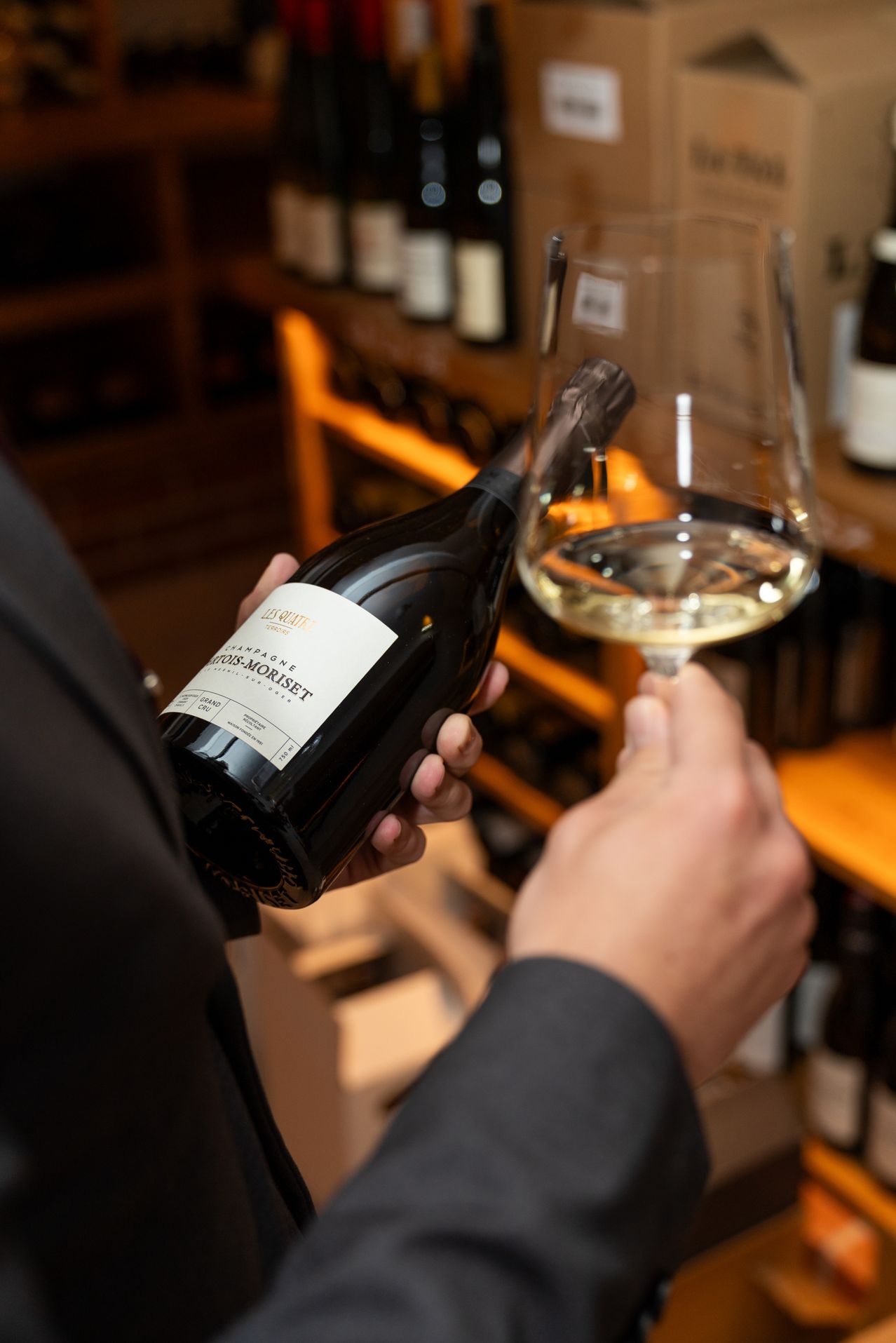 Eine Person hält eine Flasche Les Doutches Champagner mit einem Weinglas in einem Weinladen.