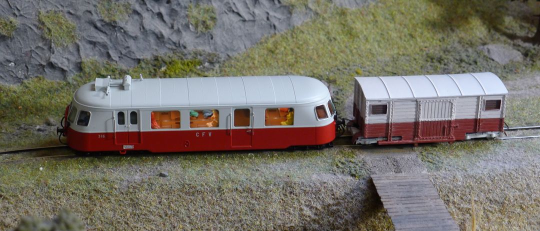 Ein Modellzug mit rotem und weißem Körper steht auf einer Schiene mit einer Holzplattform. Der Zug hat die Buchstaben CFV an seiner Seite.