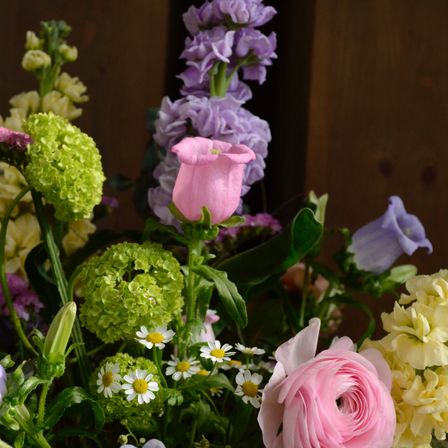 Nahaufnahme einer Blumenarrangement mit verschiedenen Blumen, darunter rosa Rosen, grüne kugelförmige Blumen und weiße Gänseblümchen, in einer natürlichen Umgebung angeordnet.