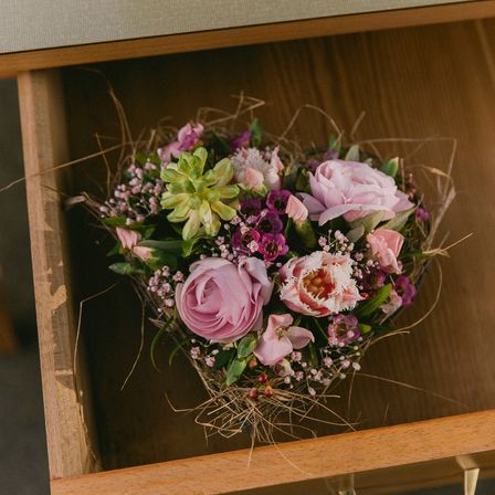 Eine Holzschublade mit einer herzförmigen Blumenanordnung, bestehend aus rosa Rosen, grünen Sukkulenten und anderen Blumen, ist in einem natürlichen und rustikalen Stil arrangiert.