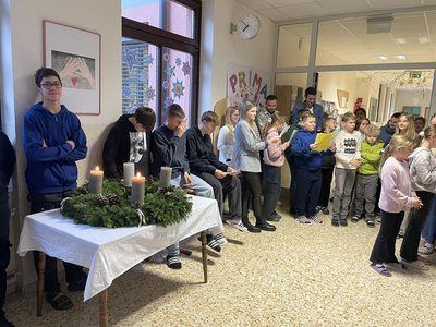 Eine Gruppe von Menschen, darunter Kinder, steht um einen Tisch mit brennenden Kerzen, möglicherweise während eines Gebets oder einer Zeremonie in einem Raum mit weißen Wänden und Glastüren.