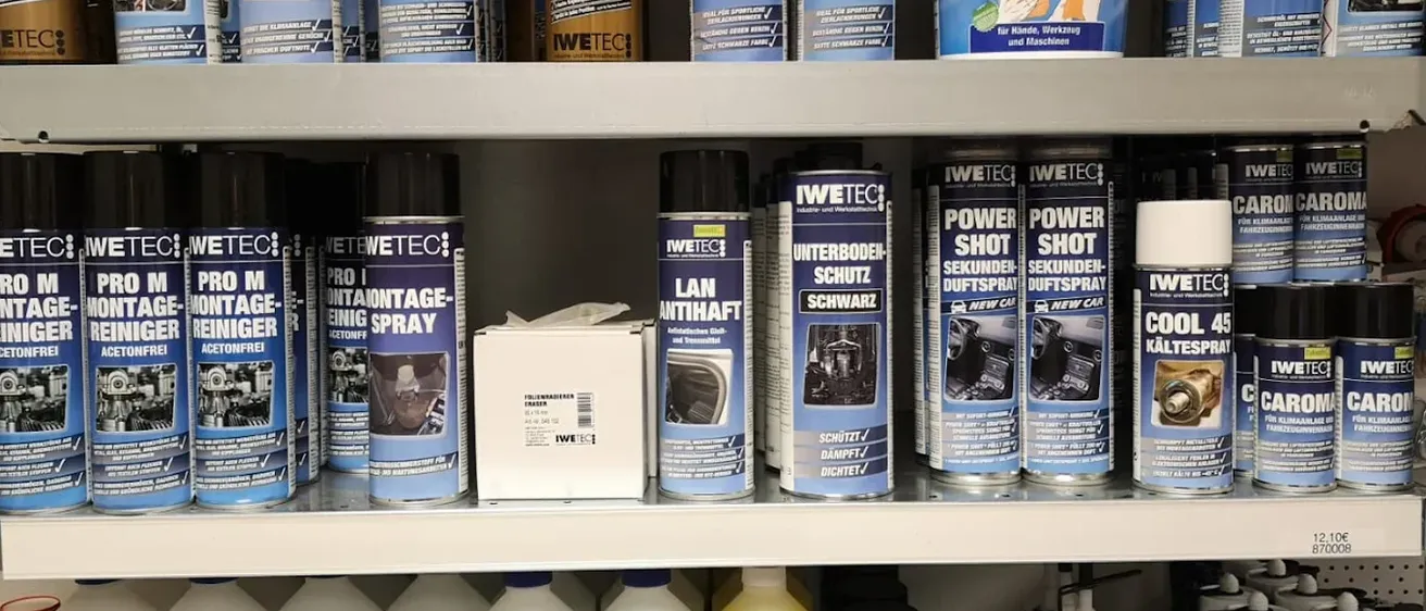 Ein Regal mit mehreren Dosen und Flaschen von Produkten, darunter Reinigungssprays und Schutzsprays. Die Produkte sind in verschiedenen Farben und Größen und einige haben Etiketten mit Text in einer Fremdsprache.