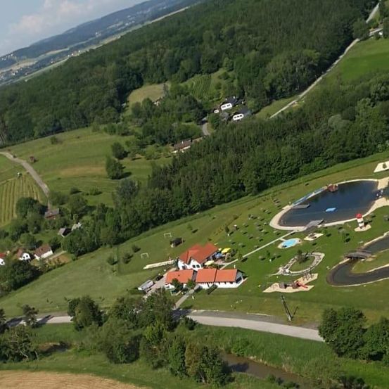 Luftaufnahme eines Erholungsgebiets mit einem See, Häusern und einer Straße, umgeben von grünen Feldern und Bäumen.