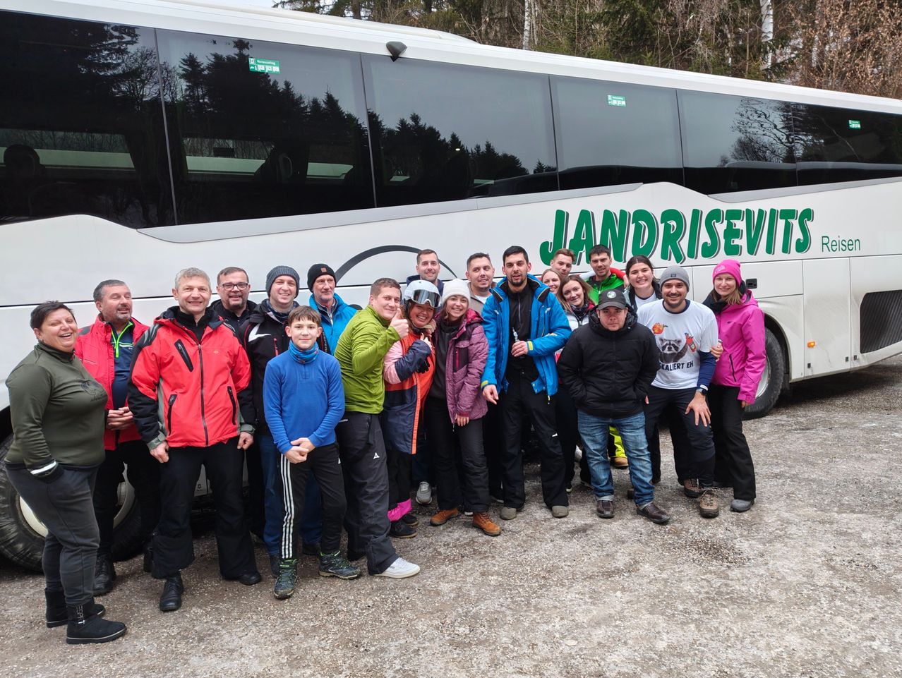 Eine Gruppe von Menschen posiert für ein Foto vor einem Bus mit dem Wort Jandrisevity. Sie tragen alle Winterkleidung.