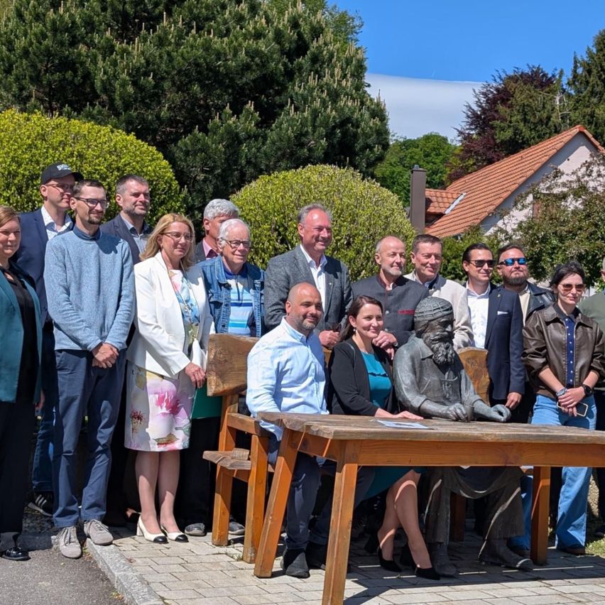 Eine Gruppe Erwachsener posiert für ein Foto mit einer Statue eines bärtigen Mannes vor einem Haus.