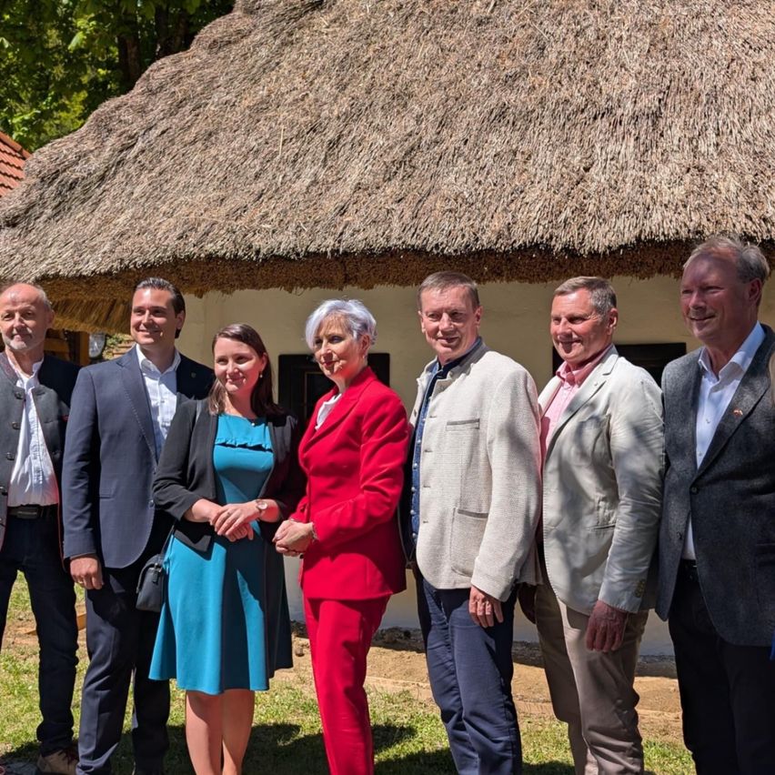 Sieben Menschen, wahrscheinlich eine Gruppe von Fachleuten, stehen lächelnd vor einer Strohdachhütte für die Kamera.