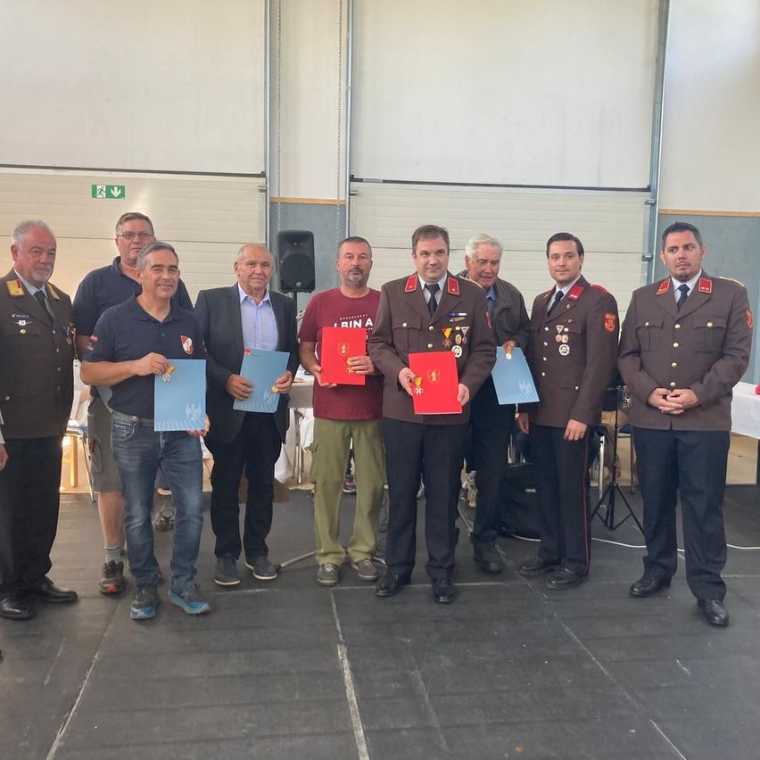 Eine Gruppe von Männern in Uniformen und Anzügen, die rote und blaue Zertifikate halten, stehen zusammen in einem Raum.
