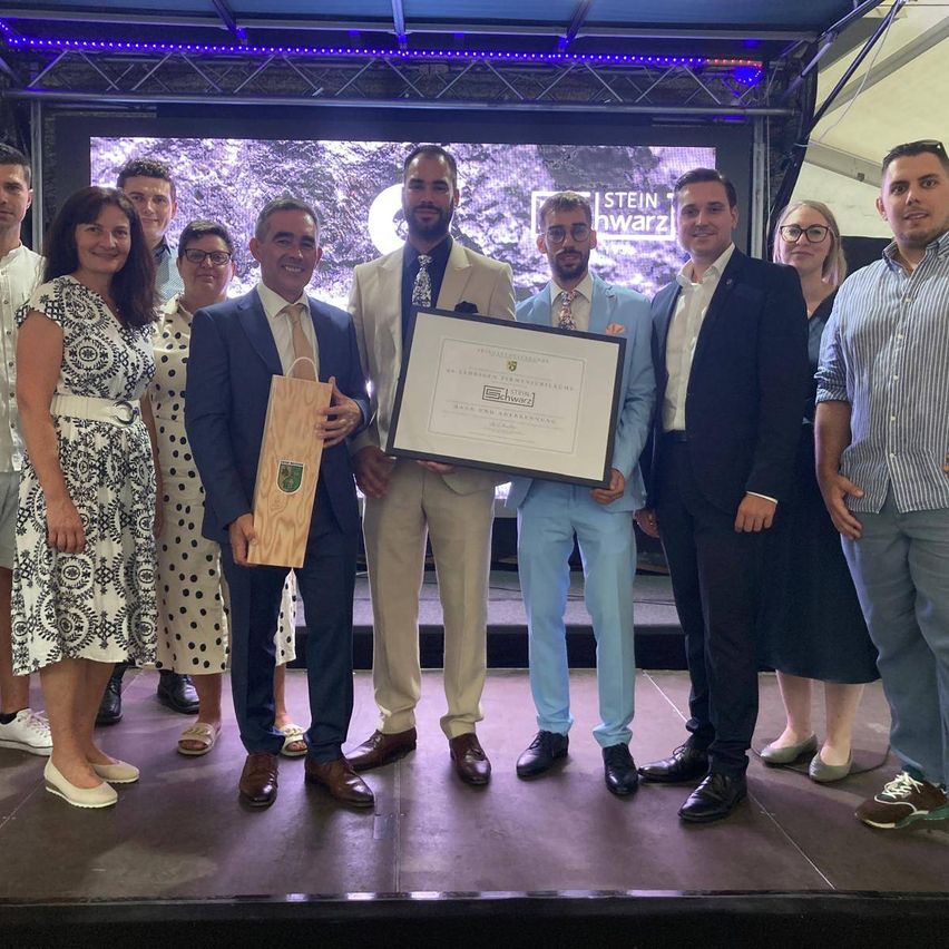 A group of people on a stage holding a plaque and smiling for a photo. The man in the center holds a wooden box.