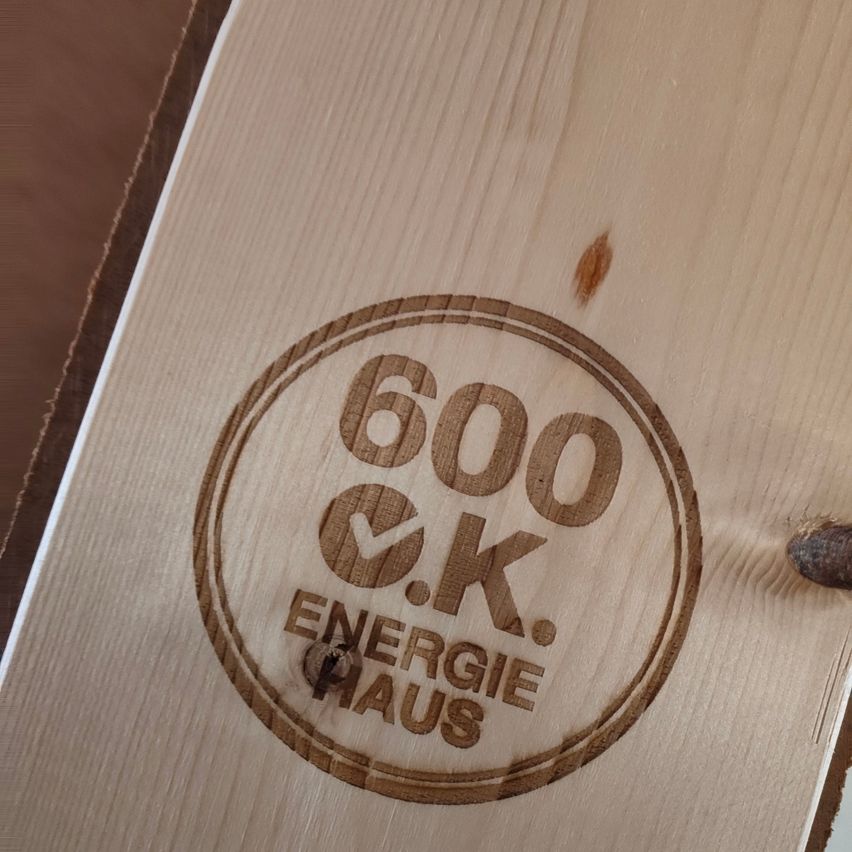 A wooden surface with a circular logo, '600 o.k. Energie Haus', burnt into it.