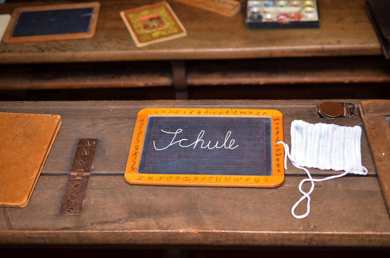 A classroom with a vintage chalkboard displaying 'Schule' and a white string on a wooden desk.