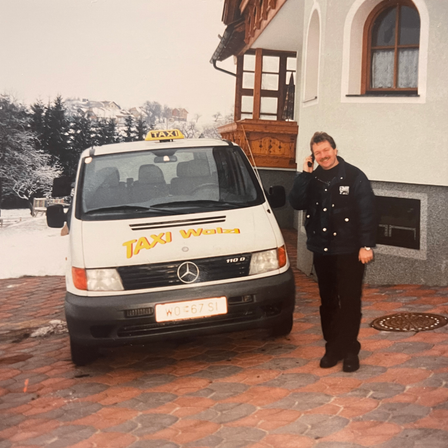 Ein Mann steht neben einem Taxi-Van mit verschneirtem Hintergrund. Der Taxi-Van hat das Wort Taxi oben.