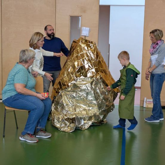 Eine Gruppe von Erwachsenen und einem Kind interagiert um ein großes goldenes Objekt in einem Raum mit Holzwänden.