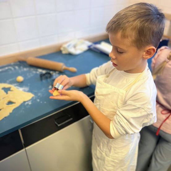 Ein junger Junge, der eine Schürze trägt, steht an einer Arbeitsplatte und verwendet einen Ausstecher auf Teig.