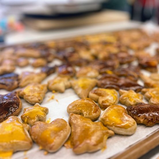 Ein Backblech gefüllt mit gebackenen Gebäckstücken in verschiedenen Formen, einschließlich Sterne, Herzen und Kreise, einige glasiert. Die Gebäckstücke haben eine goldbraune Farbe.