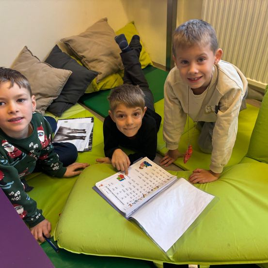 Drei Jungen sitzen auf einem grünen Sitzsack. Ein Junge hält ein Buch. Der Junge in der Mitte lächelt.