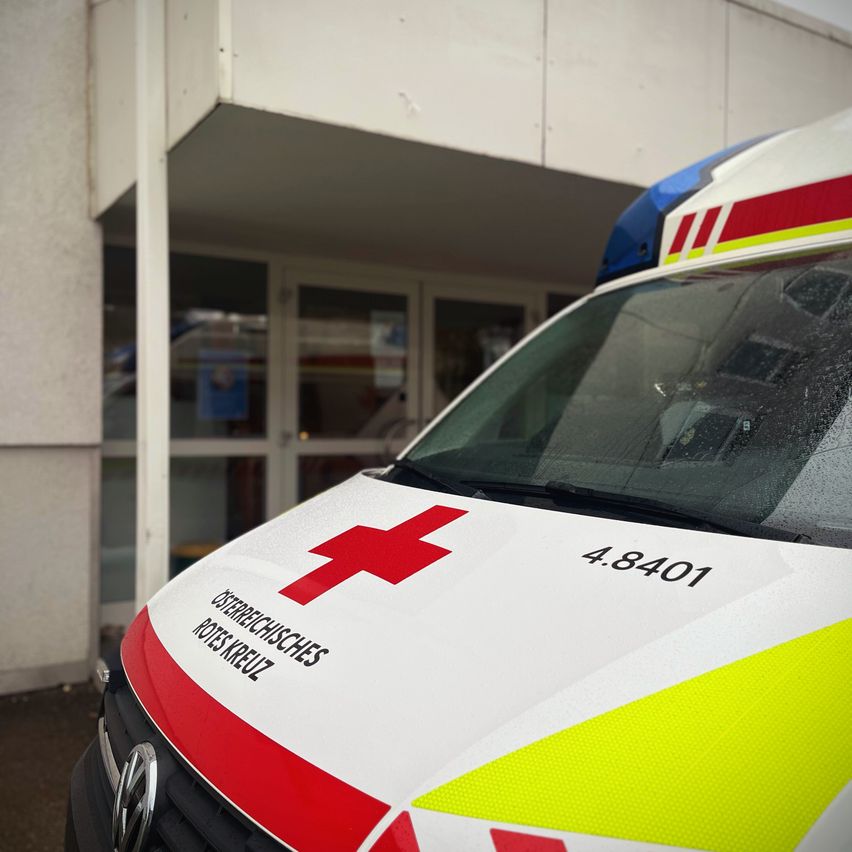 Vorderansicht eines Rettungswagens, der vor einem Gebäude mit Glastüren geparkt ist, mit einem roten Kreuz und der Nummer 4.8.401.