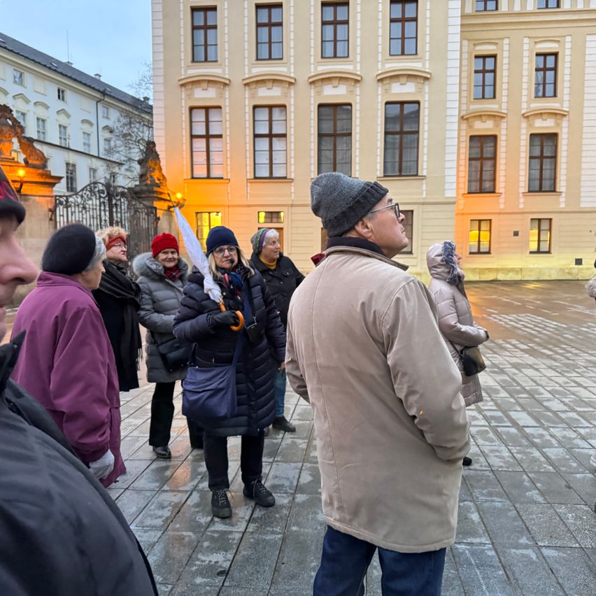 Eine Gruppe von Menschen in Winterkleidung steht vor einem großen historischen Gebäude, wobei eine Person eine Flagge hält.