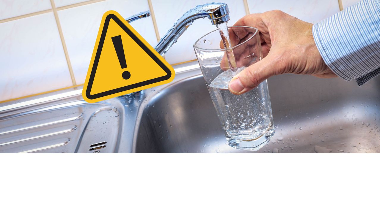 Eine Hand füllt ein Glas Wasser aus einem Wasserhahn, mit einem Warndreieck über dem Waschbecken.