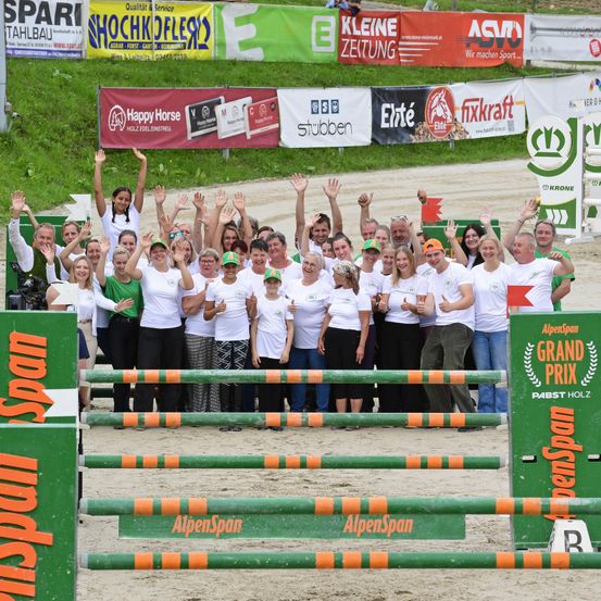 Eine Gruppe von Menschen in weißen T-Shirts und Hüten posiert für ein Foto vor einer Hindernisbahn.