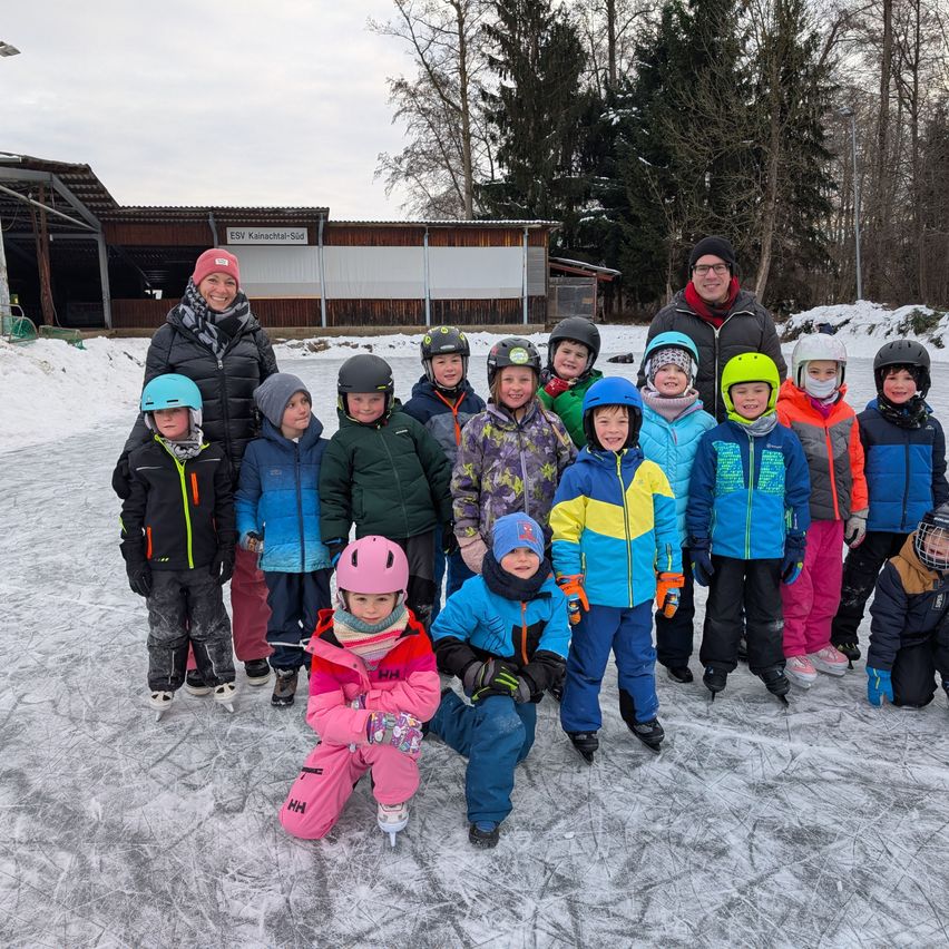 Eine Gruppe von Kindern und Erwachsenen posiert für ein Foto auf einer Eisbahn. Dahinter steht ein Gebäude mit der Aufschrift ESV Kleinmachnow Süd.
