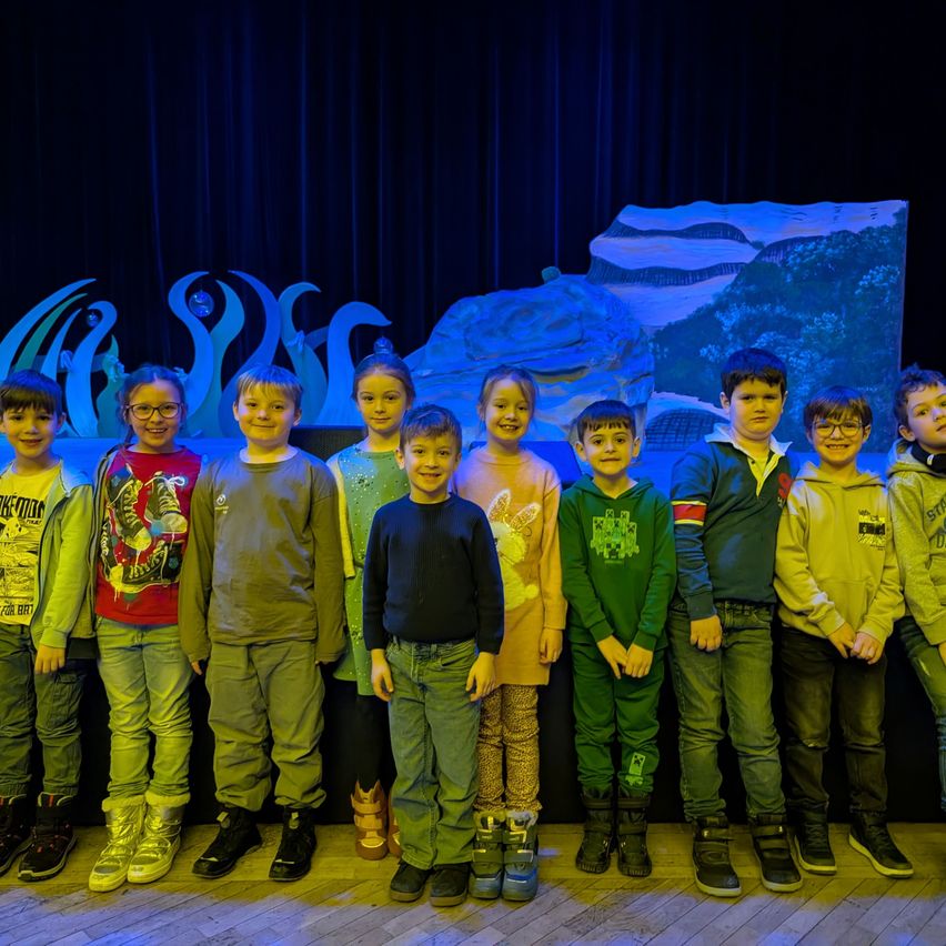 Eine Gruppe von Kindern posiert für ein Foto auf einer Bühne mit blauem Hintergrund und einer Eisskulptur im Hintergrund.