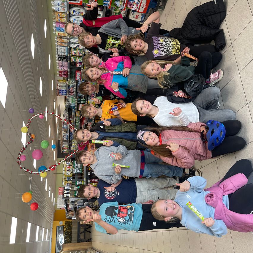 Eine Gruppe von Kindern, die lächelnd in einem hell beleuchteten Laden mit bunten Luftballons und Lichtern posiert.