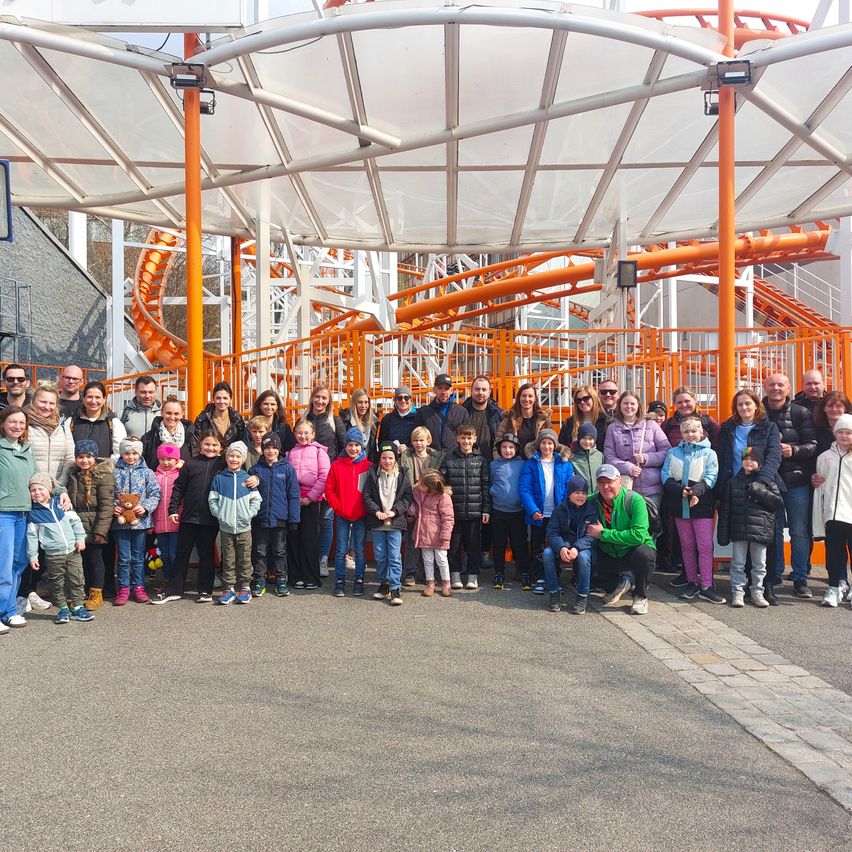 Eine Gruppe von Menschen posiert für ein Foto in einem Vergnügungspark vor einer großen Achterbahn.