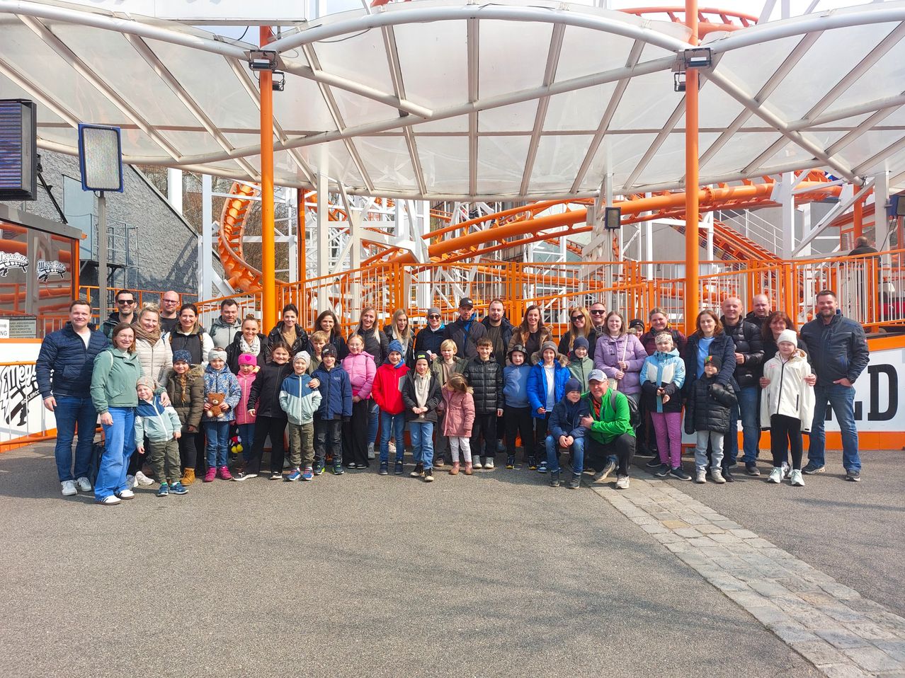Eine Gruppe von Menschen posiert für ein Foto in einem Vergnügungspark vor einer großen Achterbahn.