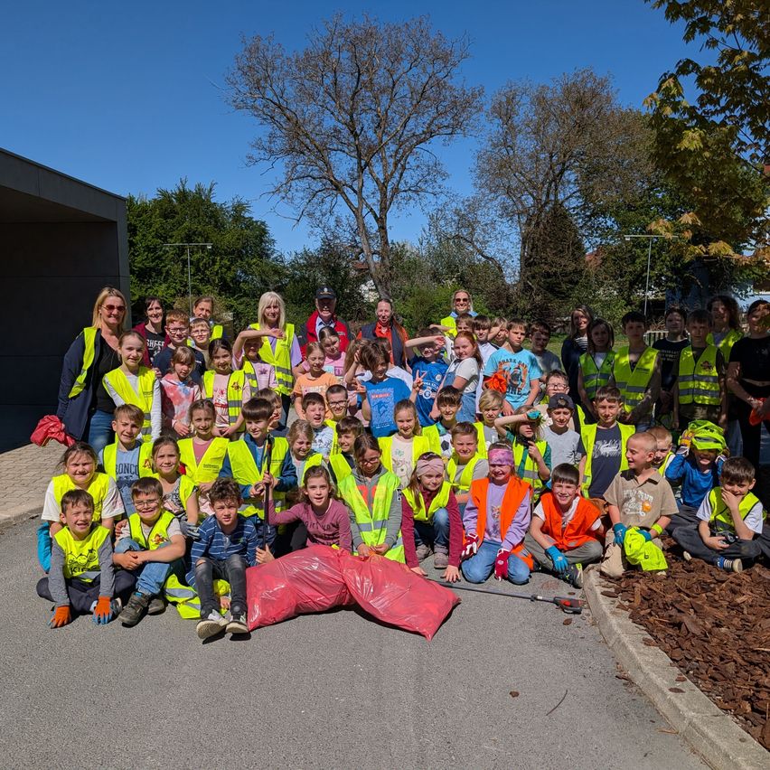Eine Gruppe von Kindern und Erwachsenen posiert für ein Foto in einem Park, alle tragen gelbe Westen und halten Plastiktüten. Einige haben Gesichtsbemalung.