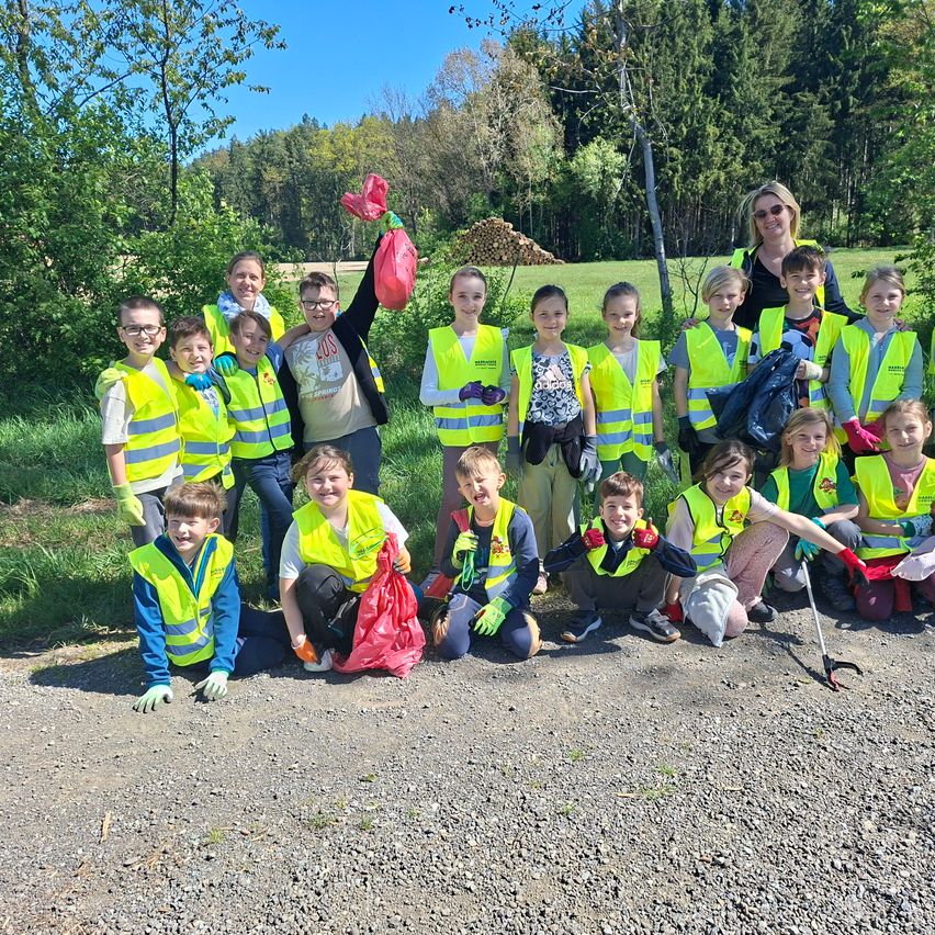 Eine Gruppe junger Kinder und Erwachsener in Warnwesten posiert mit Mülltüten für ein Foto, wahrscheinlich für eine Gemeinschaftsreinigungsveranstaltung.