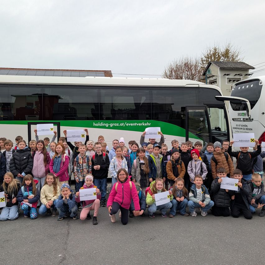 Eine Gruppe von Kindern posiert mit Schildern vor einem Bus an einem bewölkten Tag.