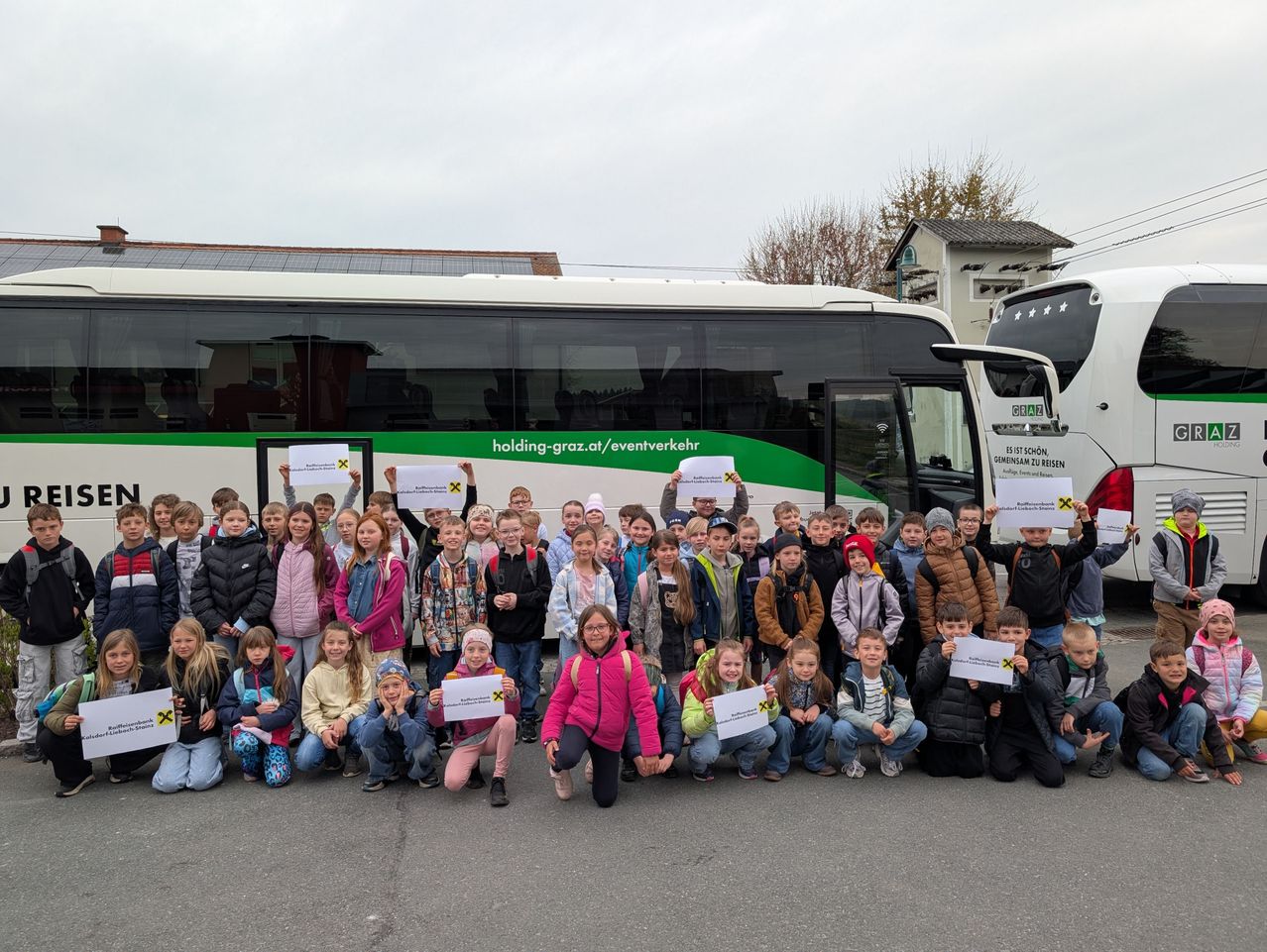 Eine Gruppe von Kindern posiert mit Schildern vor einem Bus an einem bewölkten Tag.