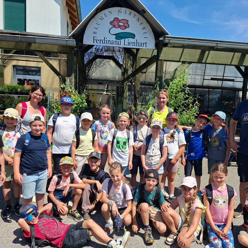 Eine Gruppe junger Kinder und zwei Erwachsene posieren für ein Foto vor einem Gebäude. Sie tragen Hüte und Rucksäcke.