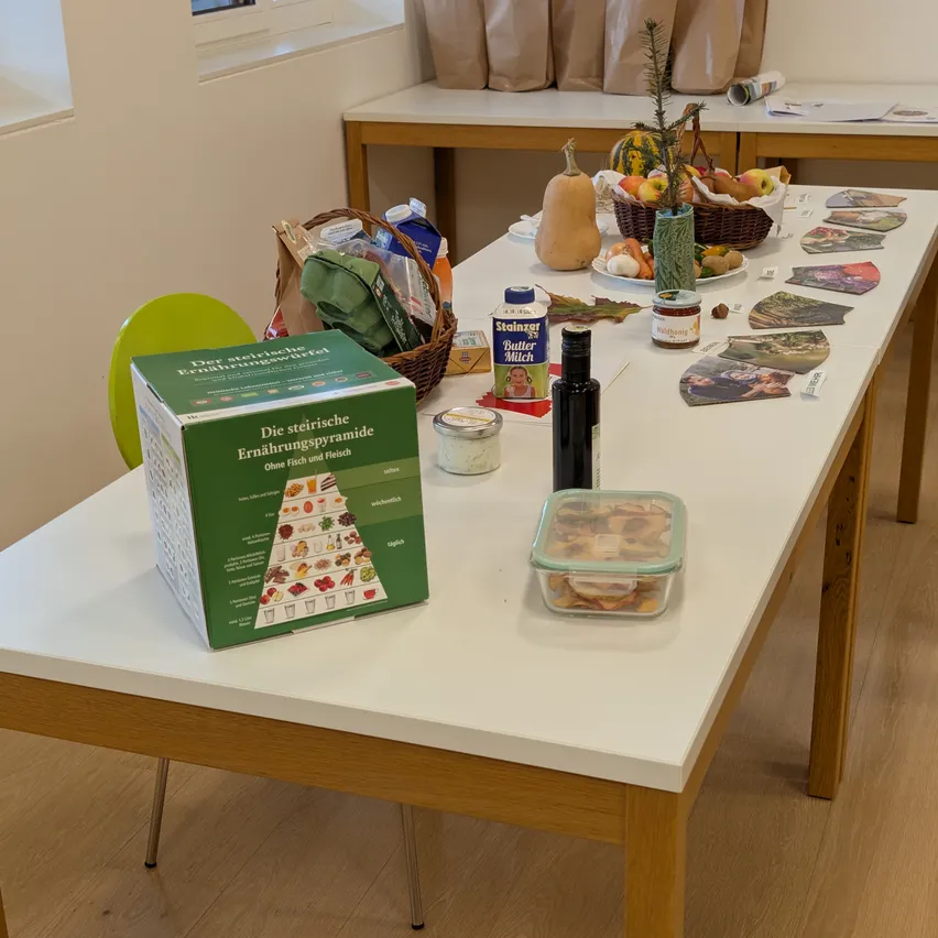 Ein Tisch mit verschiedenen Lebensmitteln und einer grünen Box mit der Aufschrift 'Die steirische Ernährungspyramide'.