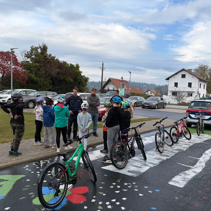 Eine Gruppe von Menschen, einige mit Helmen, versammelt sich auf einer Straße mit bemalten Fahrrädern und einem Polizeiwagen in der Nähe.