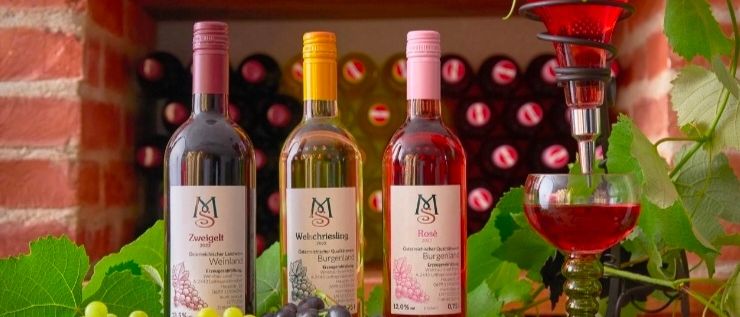 Drei Flaschen Wein und ein Glas Wein stehen auf einem Tisch mit Trauben und einem Weinpress.