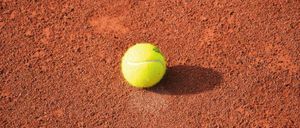 Ein Tennisball liegt auf einem roten Sandplatz.