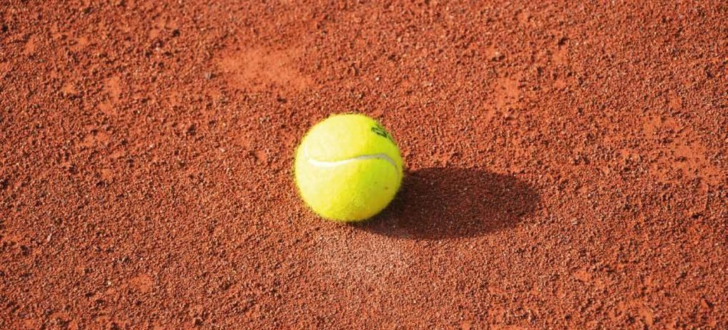 Ein Tennisball liegt auf einem roten Sandplatz.
