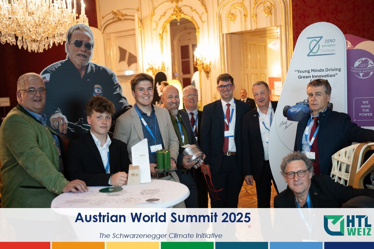 Eine Gruppe von Männern in Anzügen und Krawatten posiert für ein Foto beim Austrian World Summit 2025. Sie stehen vor einem Tisch und einem großen Poster.