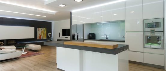 Eine moderne Küche mit weißen Schränken, einer Holzarbeitsplatte und einer schlanken Insel. Der Raum verfügt über Holzböden, einen Fernseher und einen Kühlschrank.
