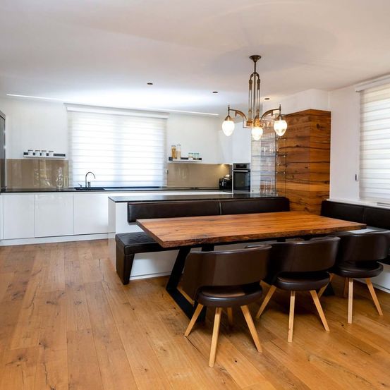Eine moderne Küche mit einem Holztisch und schwarzen Stühlen. Es hat weiße Schränke, eine Hängelampe und eine Spüle.
