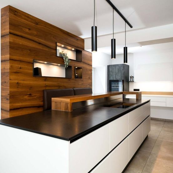 Moderne Küche mit Holzwand, schwarzer Arbeitsplatte, weißen Schränken und hängenden Lampen. Regale mit Pflanzen und eine Bank unter einem Fenster.