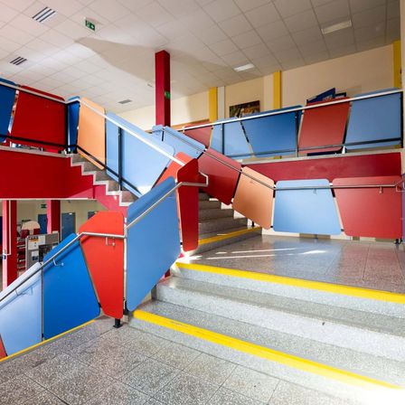 Mehrfarbige Treppe mit Handläufen in einem Gebäudeinneren. Die Treppe besteht aus verschiedenen Farben und Formen.
