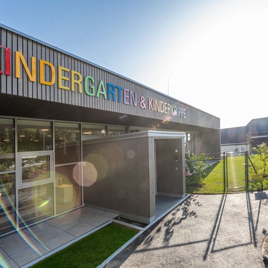 Die Vorderseite eines Kindergarten- und Kinderkrippe-Gebäudes mit bunten Buchstaben, Glasfenstern und einem Tor.