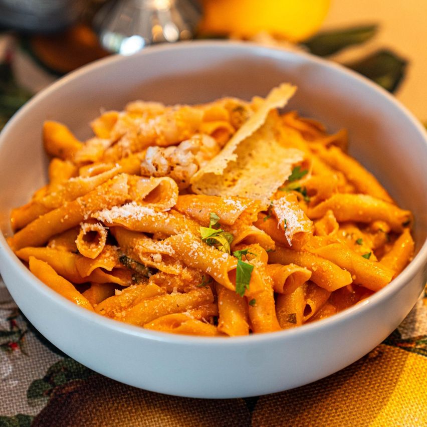 Ein weißer Teller mit cremiger Pasta, überzogen mit Käse, Kräutern und Zitronenscheiben. Das Gericht ist auf einem gemusterten Tischtuch garniert.