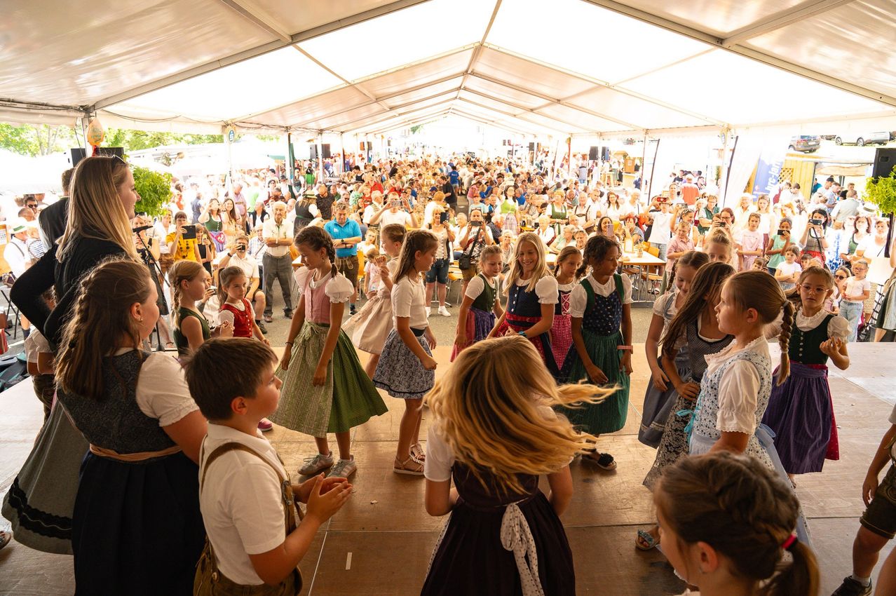 Kinder in Tracht tanzen auf einer Bühne vor einem großen Publikum in Österreich.