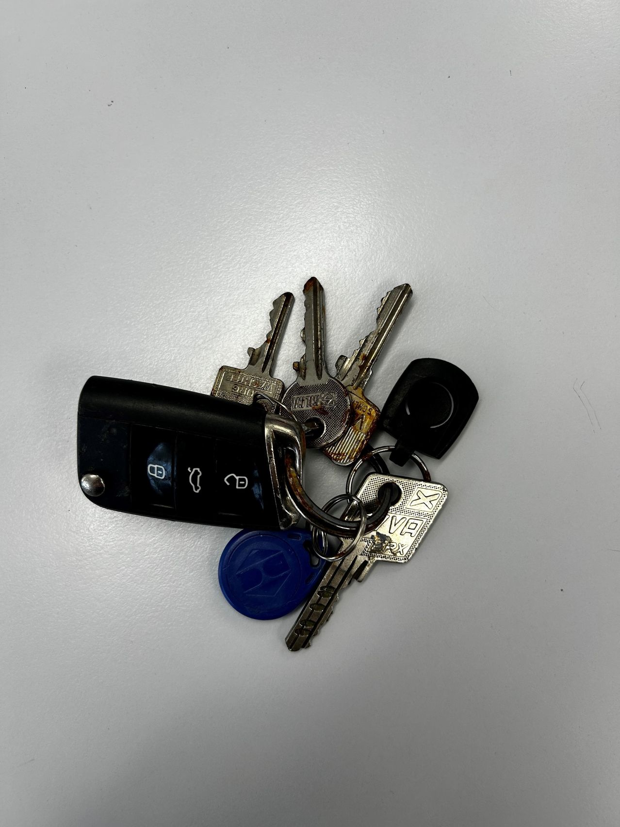 Ein Satz Autoschlüssel mit einem Schlüsselanhänger, einem blauen Schlüssel und einem schwarzen Schlüssel auf einer weißen Oberfläche.