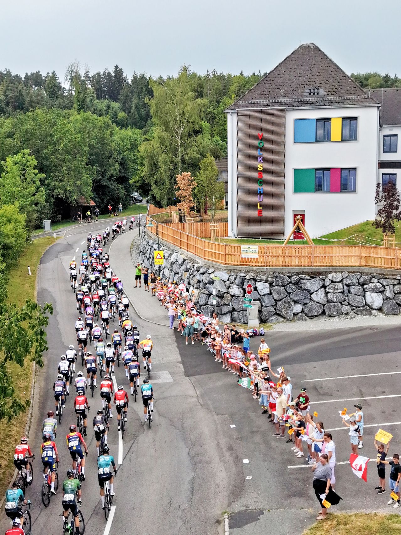 Radrennen vor Volksschule in Vorarlberg mit Zuschauern und Fahnen