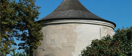 Ein Bild eines mittelalterlichen Gebäudes mit einem spitzen Dach, umgeben von Bäumen unter einem klaren blauen Himmel.