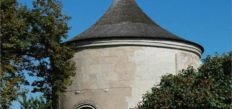 Ein Bild eines mittelalterlichen Gebäudes mit einem spitzen Dach, umgeben von Bäumen unter einem klaren blauen Himmel.